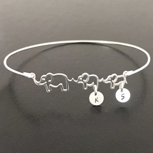 May include: A silver bangle bracelet with three elephant charms and two initial charms. The initial charms are 'K' and 'S'.