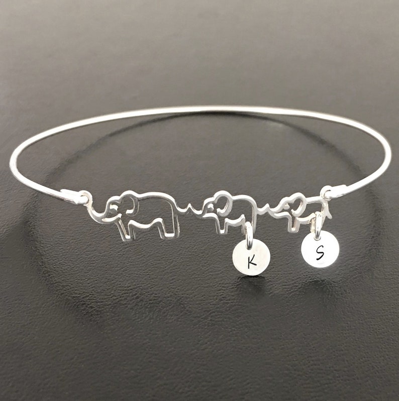 May include: A silver bangle bracelet with three elephant charms and two initial charms. The initial charms are 'K' and 'S'.