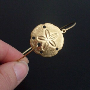 May include: A gold-toned bracelet with a sand dollar charm. The sand dollar has a five-pointed star design.