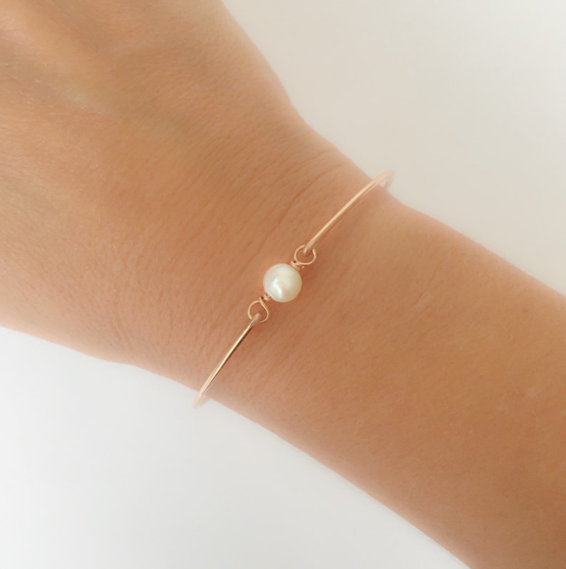 May include: A delicate rose gold bangle bracelet with a single white pearl accent.