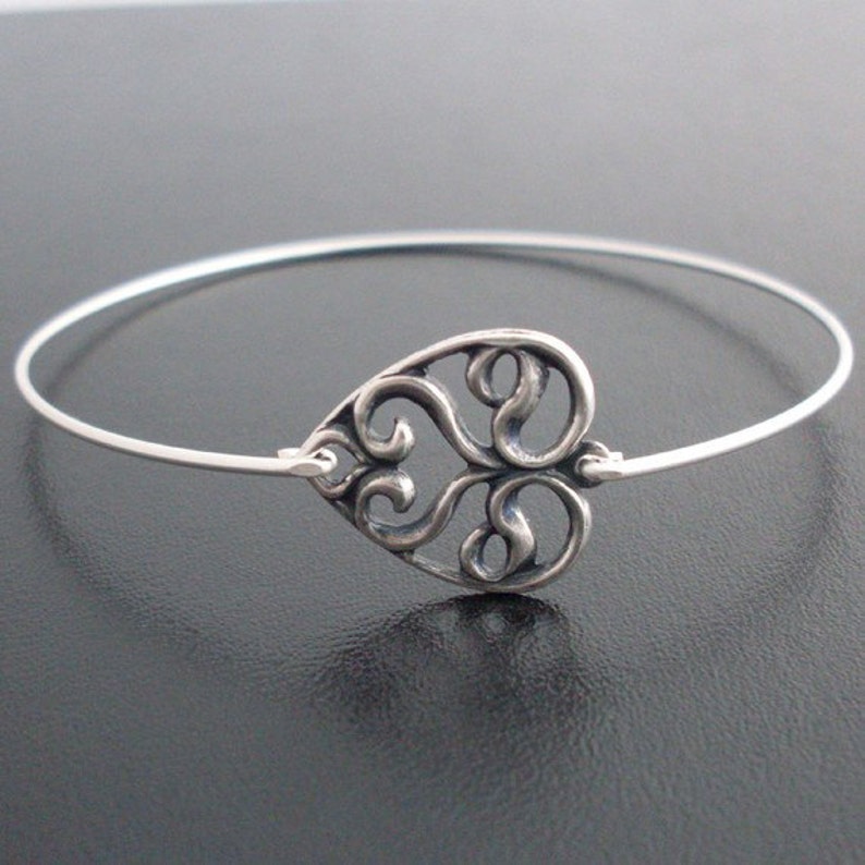 Puede incluir: Un brazalete de plata con un delicado encanto de coraz&oacute;n calado. El encanto de coraz&oacute;n est&aacute; hecho de plata y tiene un dise&ntilde;o de filigrana.