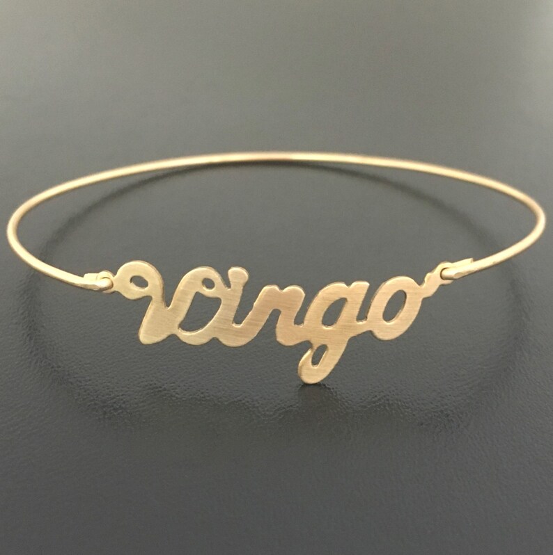 May include: A gold-toned bangle bracelet with the word "Virgo" written in a cursive script.