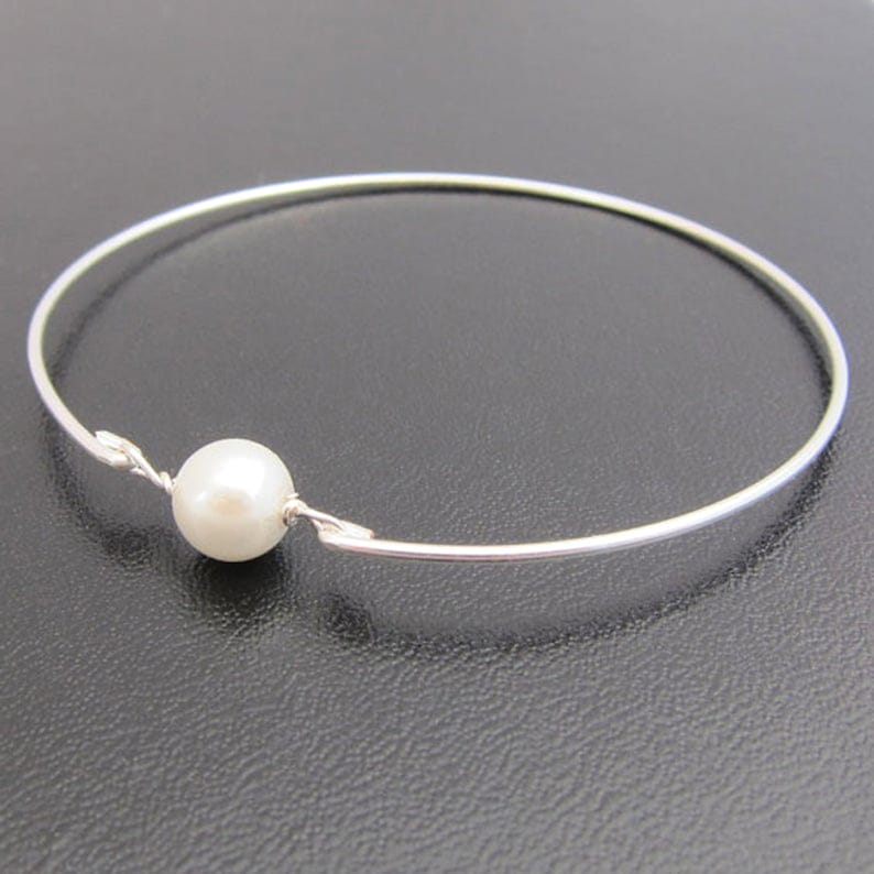 May include: A silver bangle bracelet with a single white pearl accent.