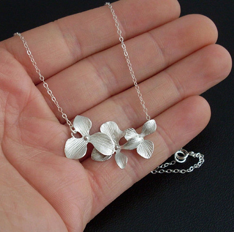May include: A silver necklace with a delicate chain and a pendant featuring three stylized flower designs.