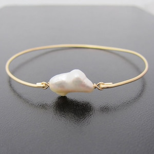 May include: A delicate gold bangle bracelet with a single large, white baroque pearl.