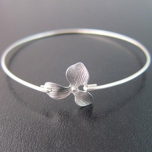 Op de afbeelding: Een zilveren armband met een delicate bloembedel. De bloembedel heeft een getextureerd oppervlak en een kleine kraal in het midden.