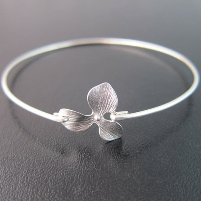 Op de afbeelding: Een zilveren armband met een delicate bloembedel. De bloembedel heeft een getextureerd oppervlak en een kleine kraal in het midden.