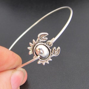 May include: A silver bangle bracelet with a silver crab charm. The crab charm has a detailed design and a shiny finish.