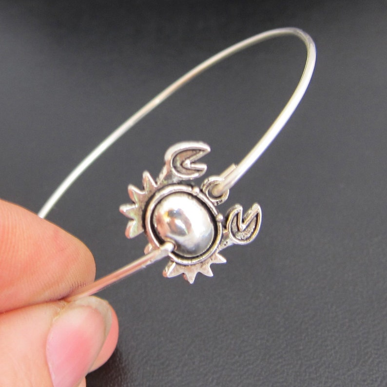 May include: A silver bangle bracelet with a silver crab charm. The crab charm has a detailed design and a shiny finish.
