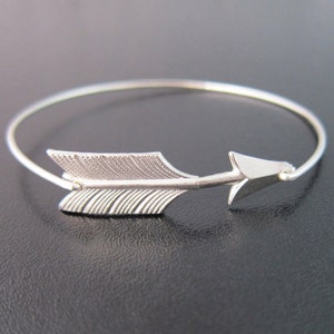 May include: A silver arrow bracelet with a delicate design. The arrow is pointing to the right and has a simple, minimalist style.