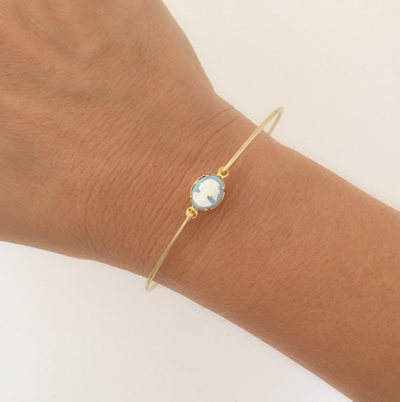 May include: A gold bangle bracelet with a light blue cameo featuring a white silhouette of a woman's profile.