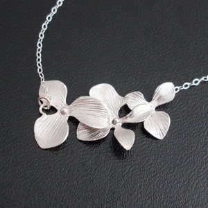 May include: Silver orchid necklace with a delicate chain. The pendant features three orchid flowers with textured petals.