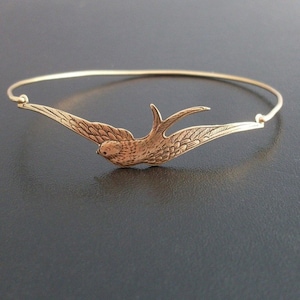 Pu&ograve; includere: Un braccialetto rigido color oro con un uccello dettagliato in volo. L'uccello ha le ali spiegate e dettagli intricati delle piume. Il braccialetto &egrave; un design semplice ed elegante, perfetto per l'uso quotidiano.
