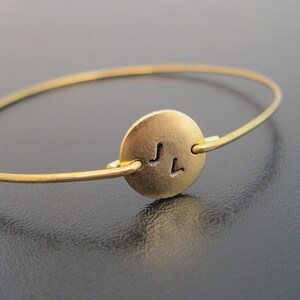 May include: A gold bangle bracelet with a round charm engraved with the initials "JL".