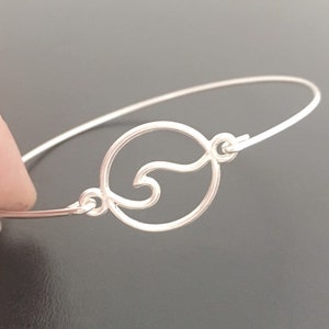 May include: A silver bangle bracelet with a wave design. The wave is cut out of a circle.