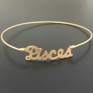 May include: Gold-toned bangle bracelet with the word "Pisces" written in a cursive font.