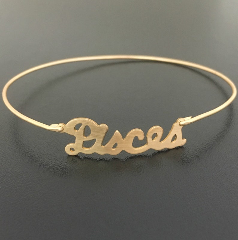 May include: Gold-toned bangle bracelet with the word "Pisces" written in a cursive font.