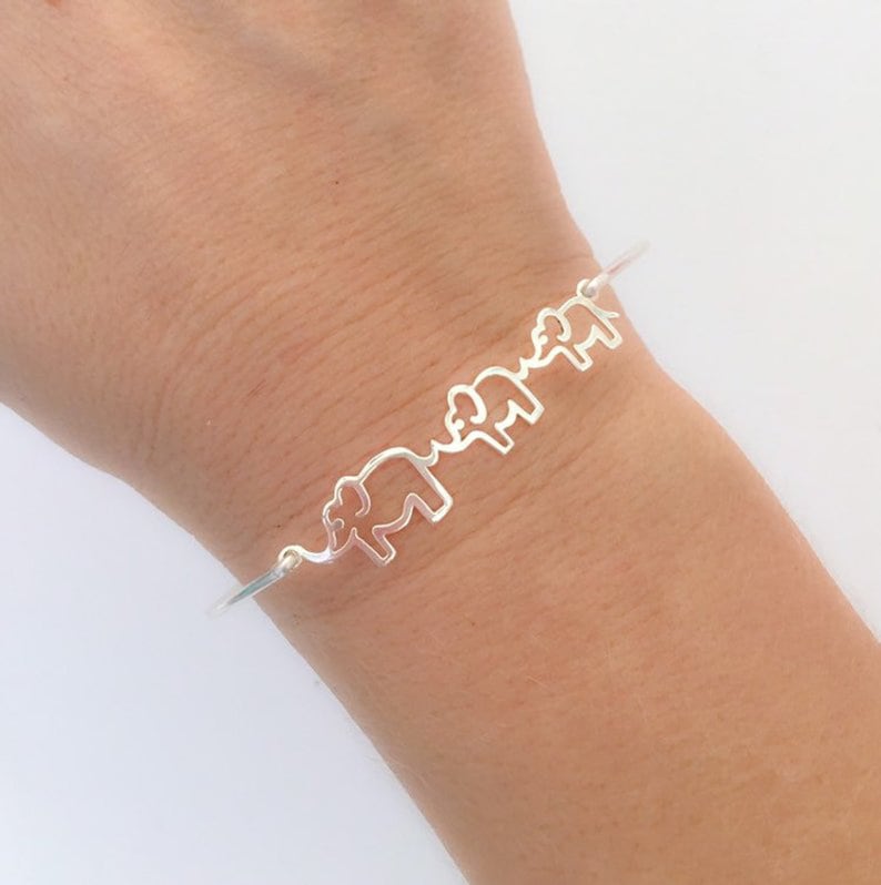 Puede incluir: Un brazalete de plata con un dise&ntilde;o de cuatro elefantes caminando en l&iacute;nea.