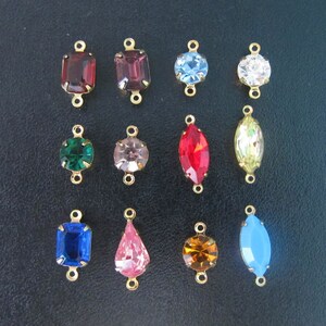 May include: Assortment of 14 gold-tone connector charms with various colored glass stones. The charms feature different shapes, including square, round, oval, and teardrop.