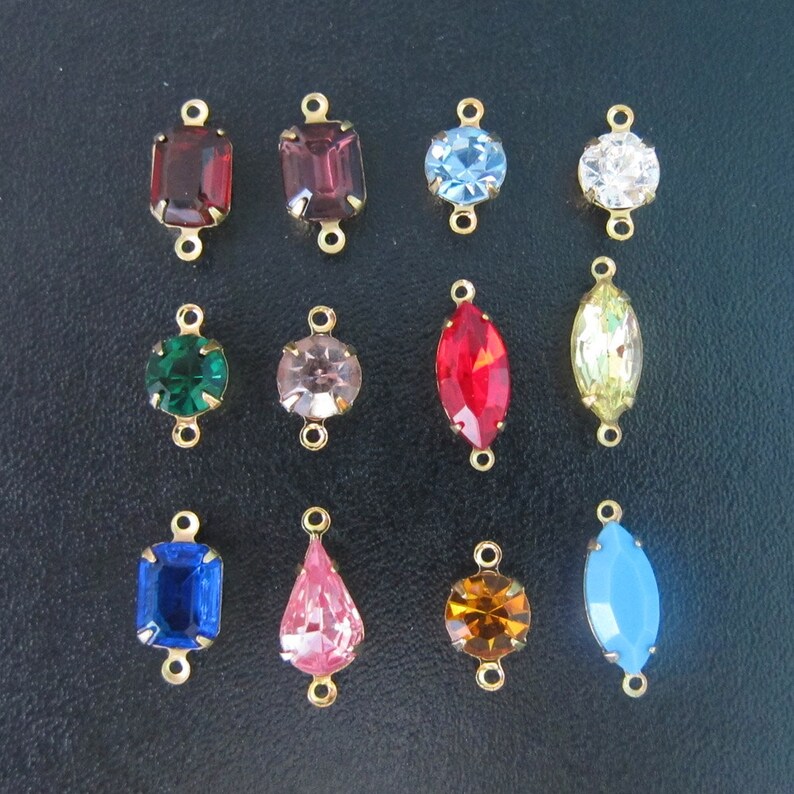 May include: Assortment of 14 gold-tone connector charms with various colored glass stones. The charms feature different shapes, including square, round, oval, and teardrop.