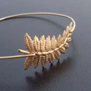 May include: A gold-toned fern leaf charm bracelet. The bracelet is made of thin wire and features a delicate fern leaf design.