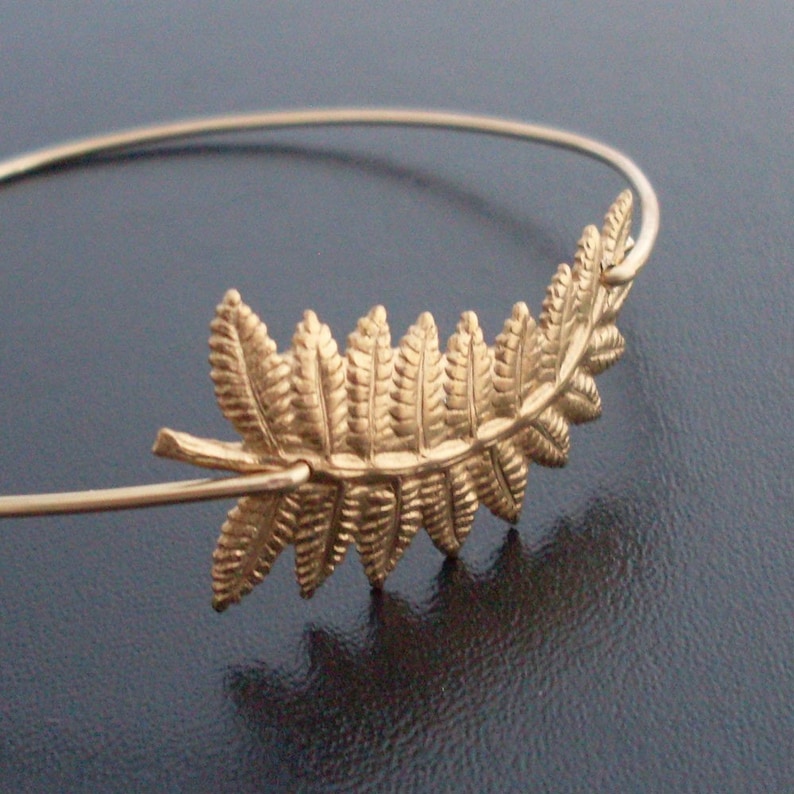 May include: A gold-toned fern leaf charm bracelet. The bracelet is made of thin wire and features a delicate fern leaf design.