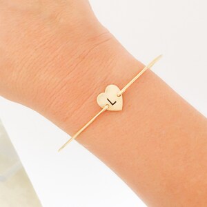 Puede incluir: Un brazalete de oro con un dije en forma de coraz&oacute;n con la letra "L" grabada.