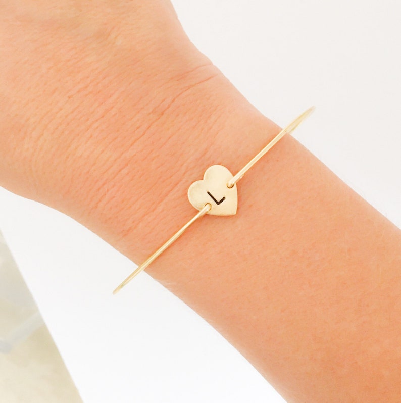 Puede incluir: Un brazalete de oro con un dije en forma de coraz&oacute;n con la letra "L" grabada.