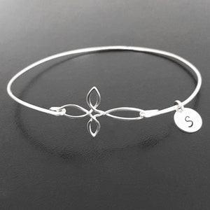 May include: A silver bangle bracelet with a Celtic knot design and a charm with the letter "S" on it.