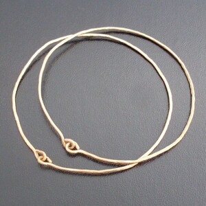 May include: Two gold-toned metal hoops, one slightly larger than the other, are stacked on top of each other. The hoops are smooth and have a slightly hammered texture.