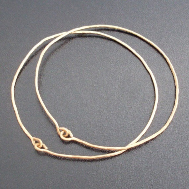 May include: Two gold-toned metal hoops, one slightly larger than the other, are stacked on top of each other. The hoops are smooth and have a slightly hammered texture.