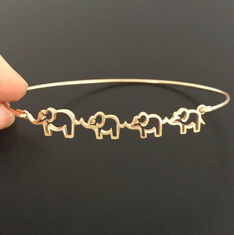 May include: A gold bangle bracelet with four elephant cutouts. The elephants are facing the same direction and are connected by their tails.