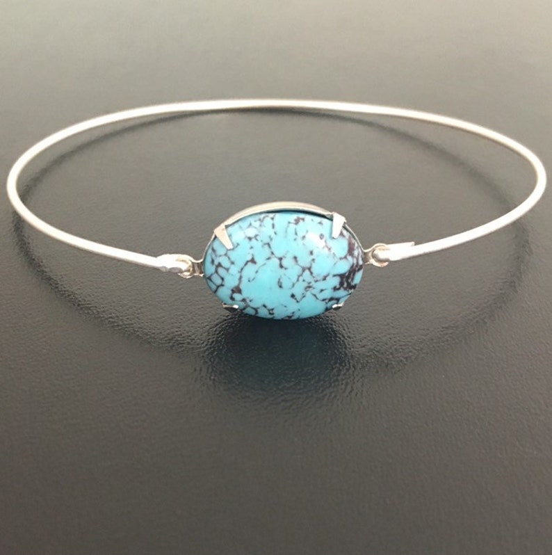 May include: A silver bangle bracelet with a turquoise oval-shaped stone set in the centre.