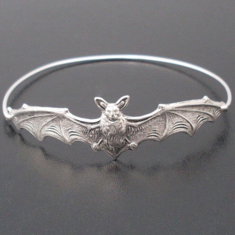 Pu&ograve; includere: Un braccialetto rigido in argento con un ciondolo a forma di pipistrello dettagliato. Il pipistrello &egrave; in volo con le ali spiegate.