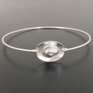 May include: A silver bracelet with a charm in the shape of a cowboy hat.