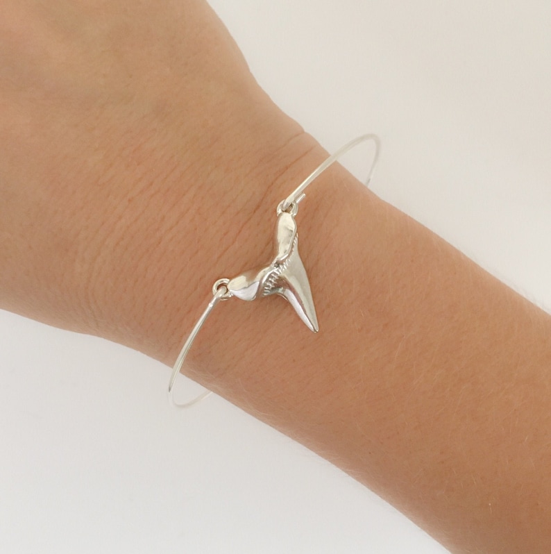 May include: A silver bangle bracelet with a shark tooth charm. The tooth is detailed and realistic.