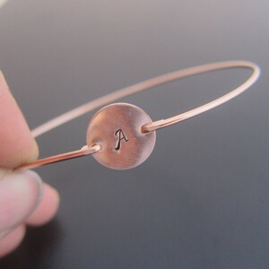 Op de afbeelding: Een ros&eacute;gouden armband met een ronde schijf bedel gegraveerd met de letter "A".