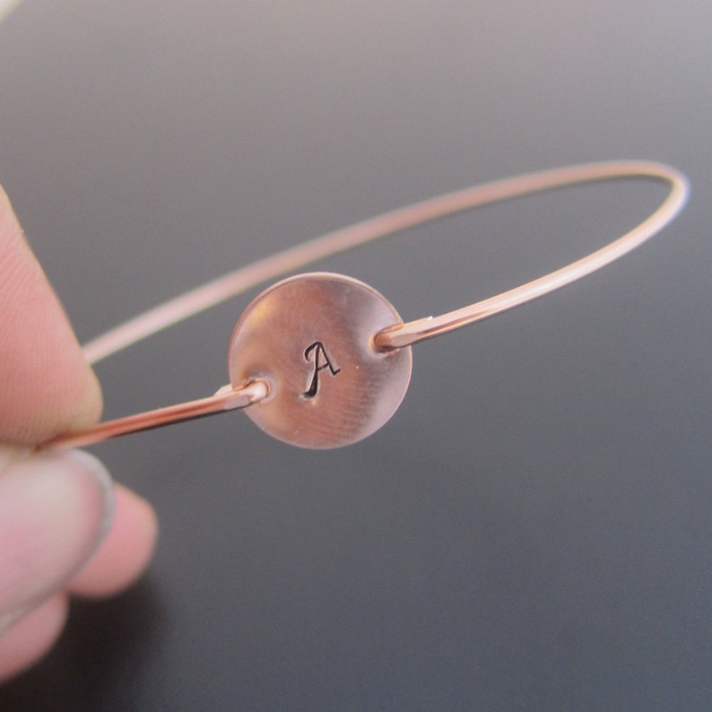 Op de afbeelding: Een ros&eacute;gouden armband met een ronde schijf bedel gegraveerd met de letter "A".