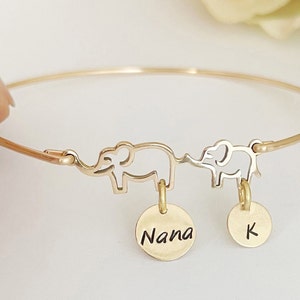 May include: Gold bangle bracelet with two elephant charms and two round charms. The larger charm says "Nana" and the smaller charm says "K".