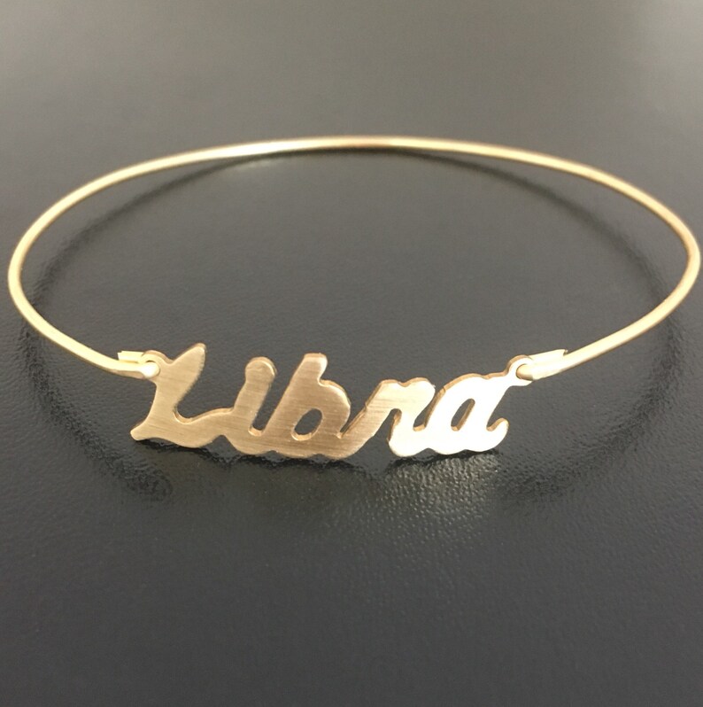 May include: Gold-toned bangle bracelet with the word "Libra" written in a cursive font.