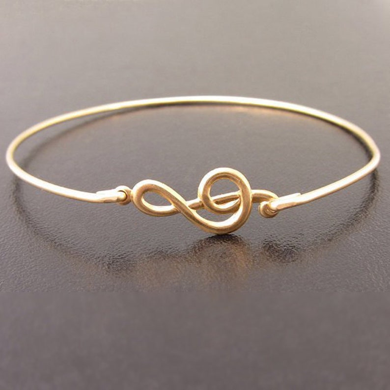 May include: A gold-toned bangle bracelet with a treble clef charm. The bracelet is thin and delicate.