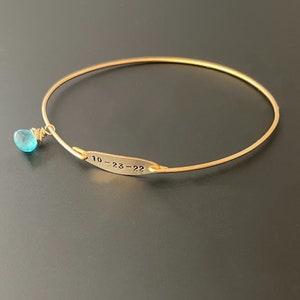 Pu&ograve; includere: Braccialetto rigido in oro con un ciondolo in pietra turchese blu e un piccolo cartellino inciso con la scritta "10-23-22".
