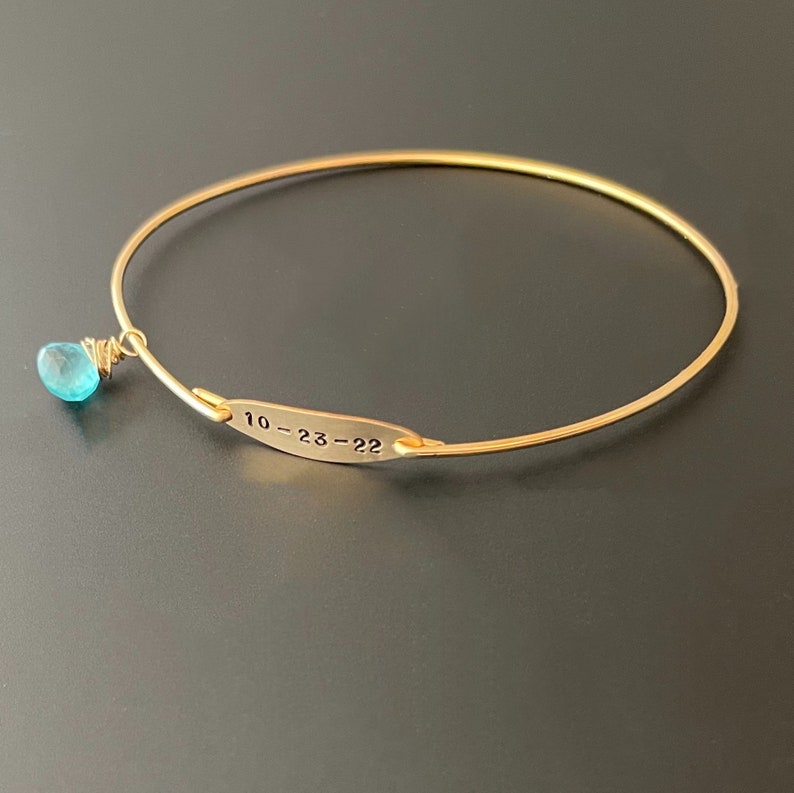 Pu&ograve; includere: Braccialetto rigido in oro con un ciondolo in pietra turchese blu e un piccolo cartellino inciso con la scritta "10-23-22".