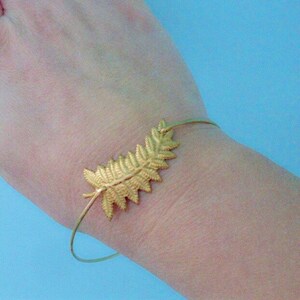 May include: A gold-toned bracelet with a delicate fern leaf design. The bracelet is open and adjustable.