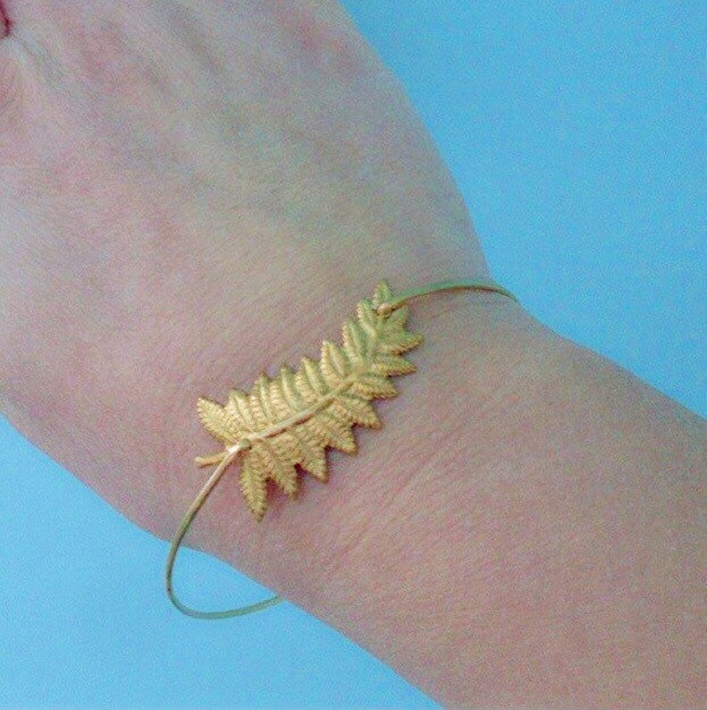 May include: A gold-toned bracelet with a delicate fern leaf design. The bracelet is open and adjustable.