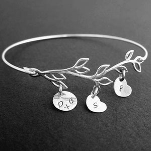 May include: Silver bangle bracelet with a delicate branch design and three charms. The charms are a heart with the letter "F", a round charm with "D+B" and a heart charm with the letter "S".