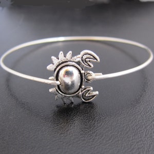 May include: A silver bangle bracelet with a crab charm. The crab is detailed with a round body and claws.