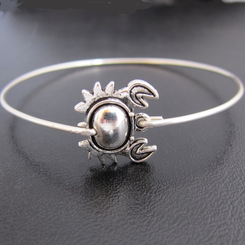 May include: A silver bangle bracelet with a crab charm. The crab is detailed with a round body and claws.