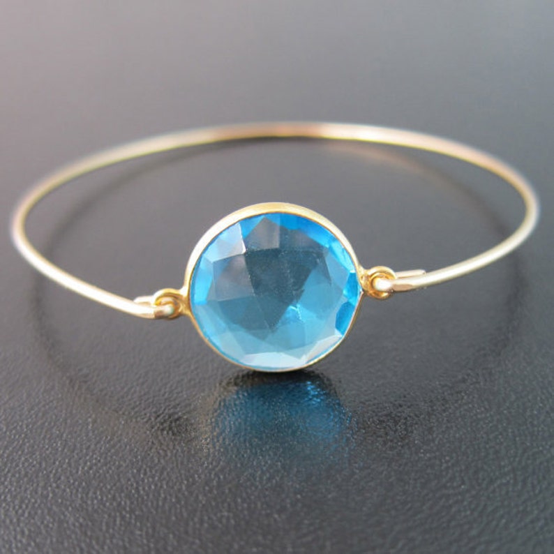 May include: A gold bangle bracelet with a large, round, light blue gemstone.