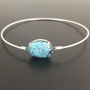 May include: A silver bangle bracelet with a turquoise oval-shaped stone set in the centre.
